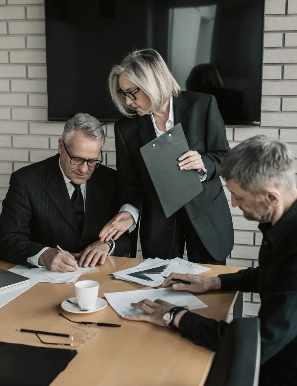 Três profissionais em uma reunião de trabalho, analisando documentos em volta de uma mesa